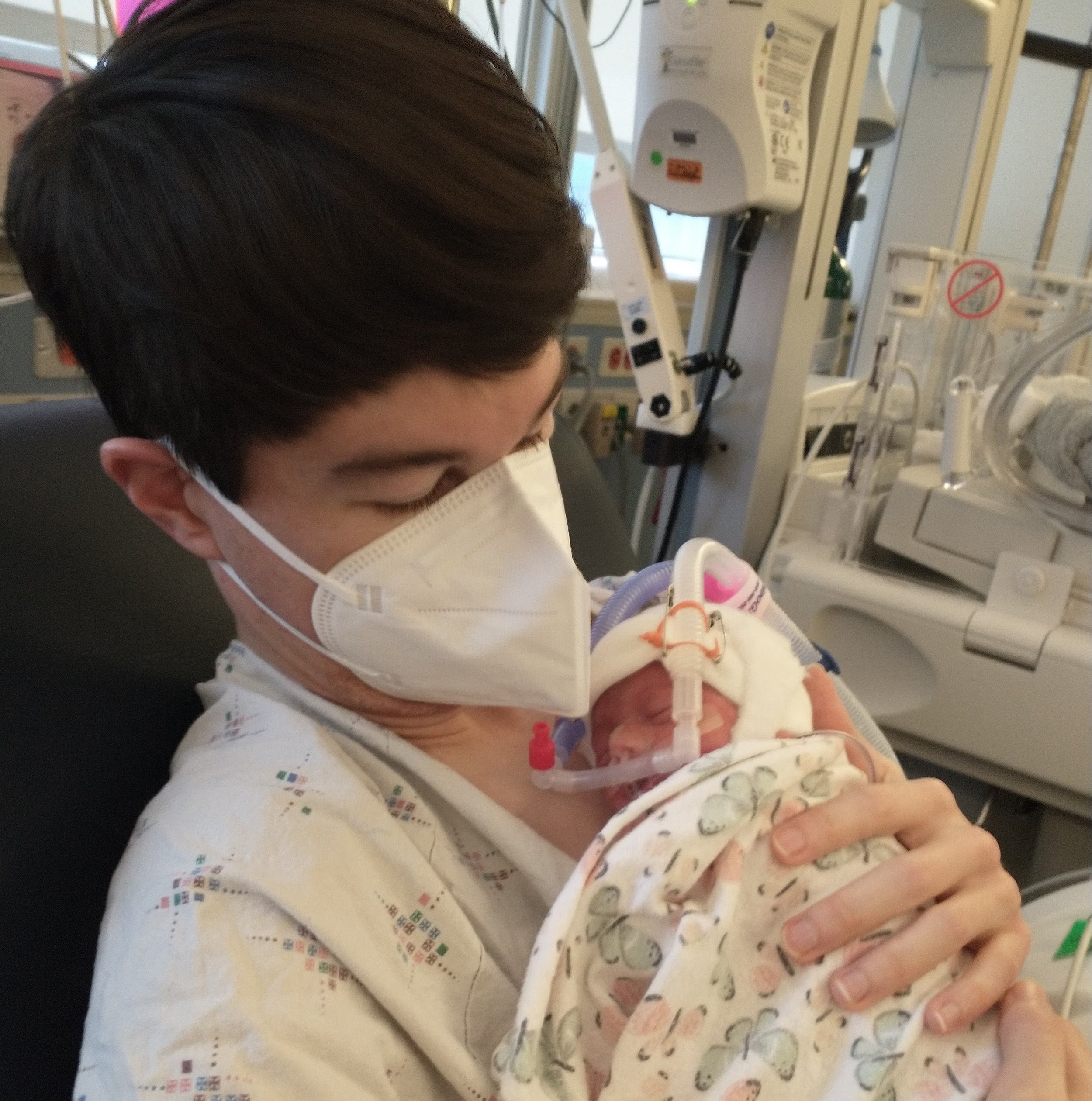 Father holding newborn infant with CPAP and monitoring equipment
